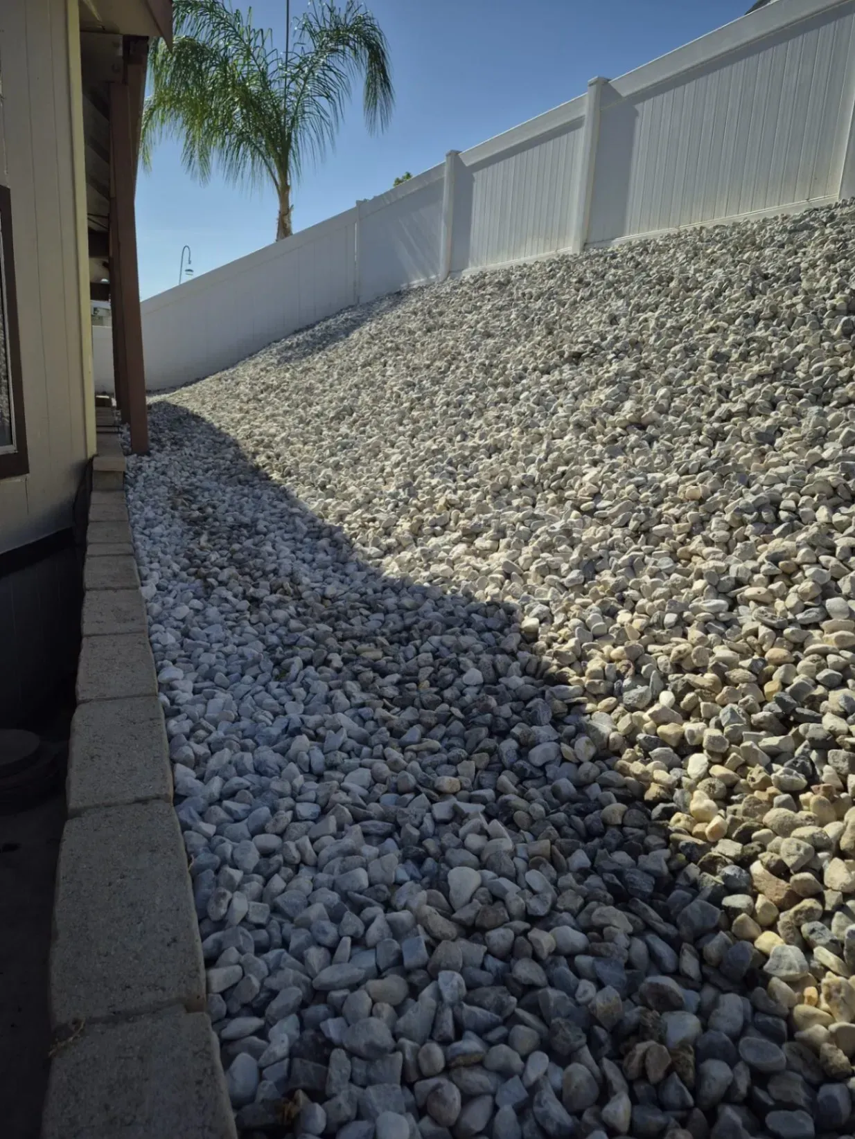 White rock-covered hillside along a white fence. A building is on the left.