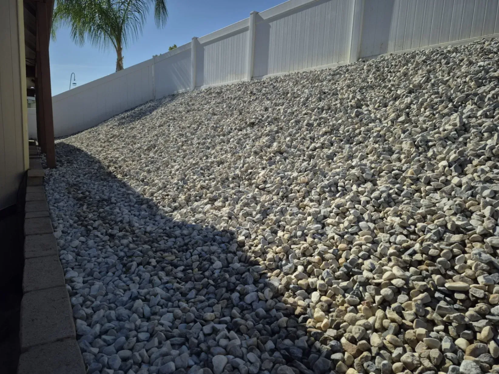 Gravel-covered slope next to a white fence and a building.