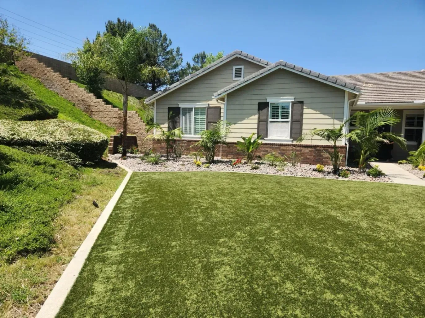 A small house with green siding and artificial turf lawn on a sunny day.