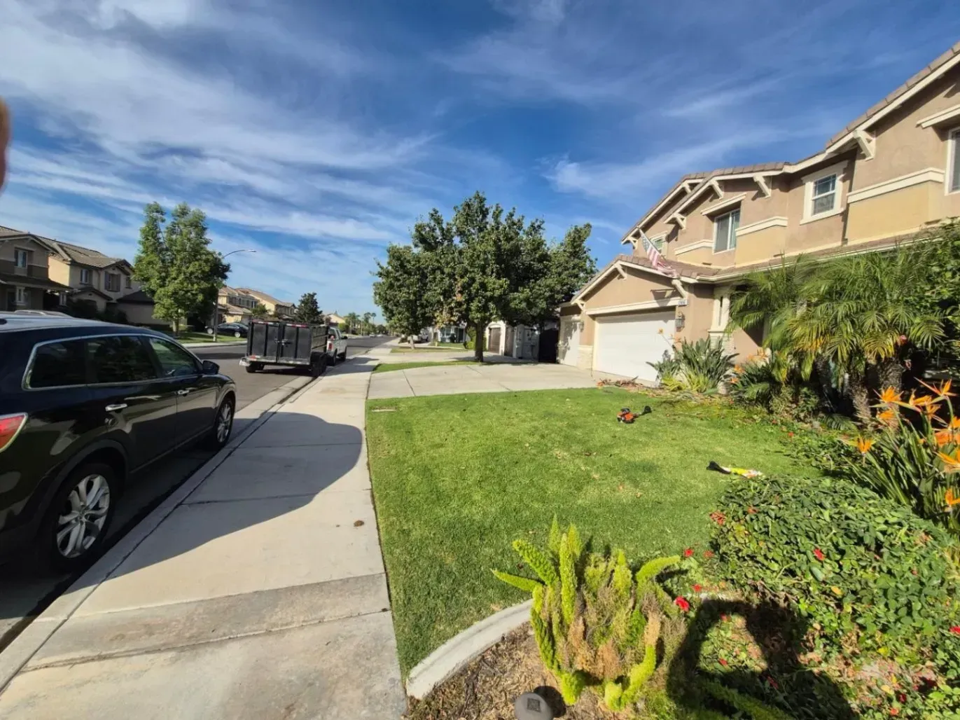 Suburban house with green lawn, sidewalk, parked car, tree, and blue sky.