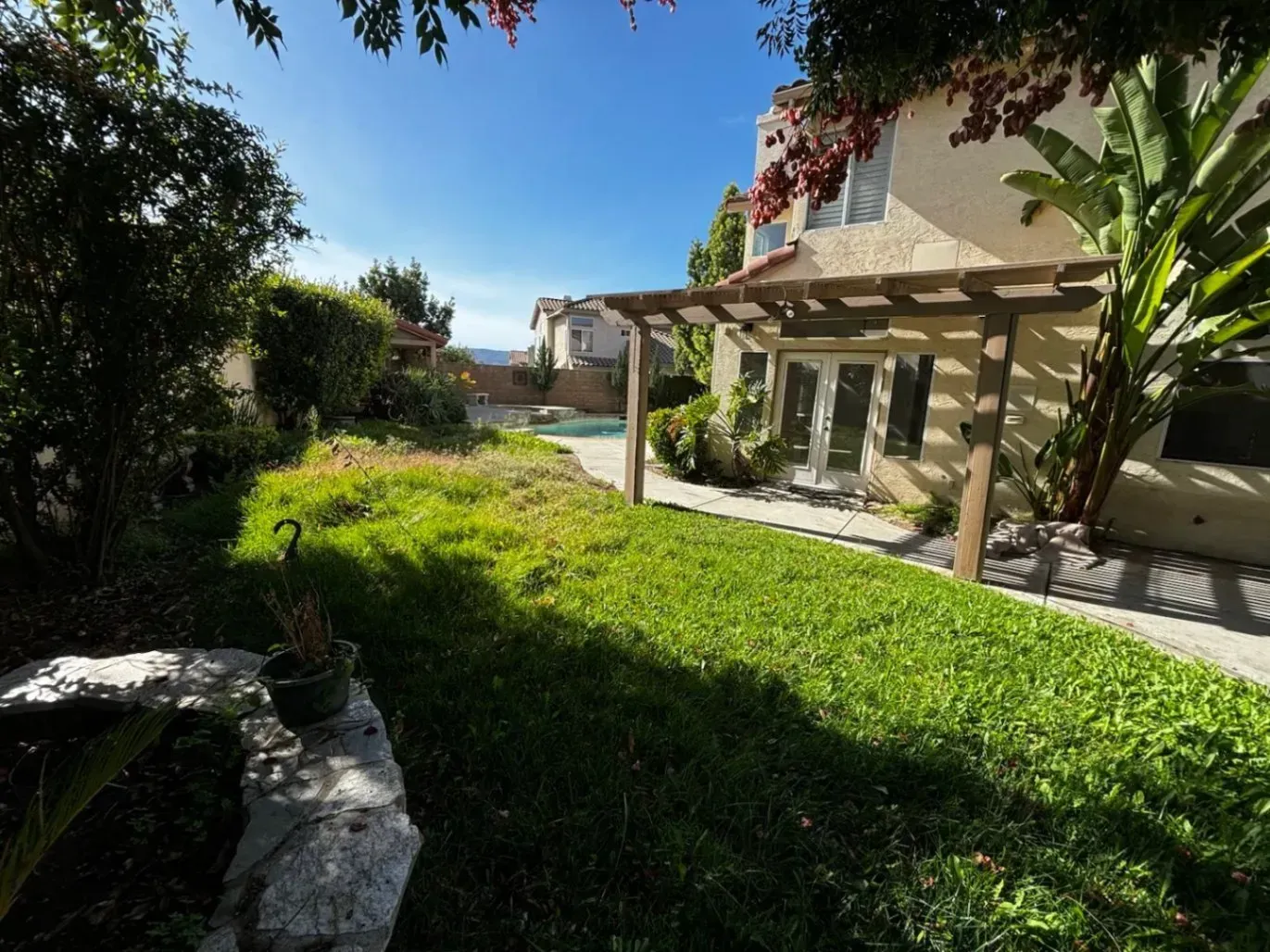 Lush green yard with a house, pergola, and pool under a bright blue sky.