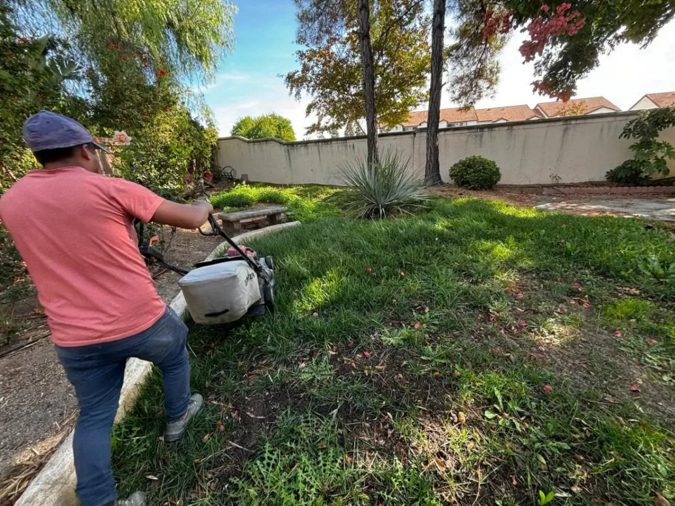 Man mowing a grassy backyard with a lawnmower on a sunny day.