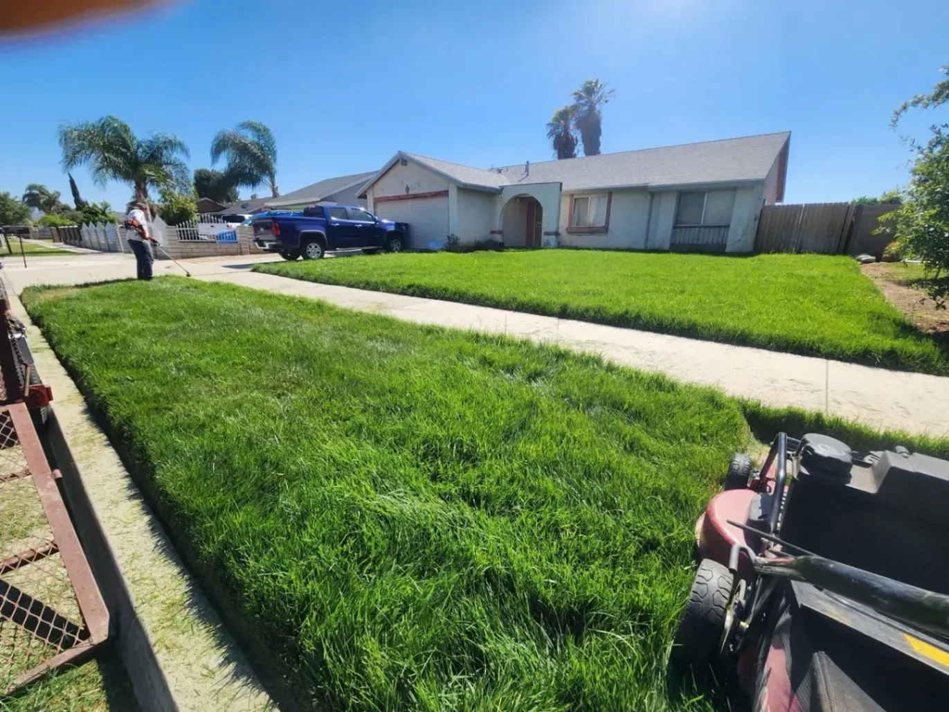 Lawn being mowed in front of a house on a sunny day. A truck is parked in the driveway.