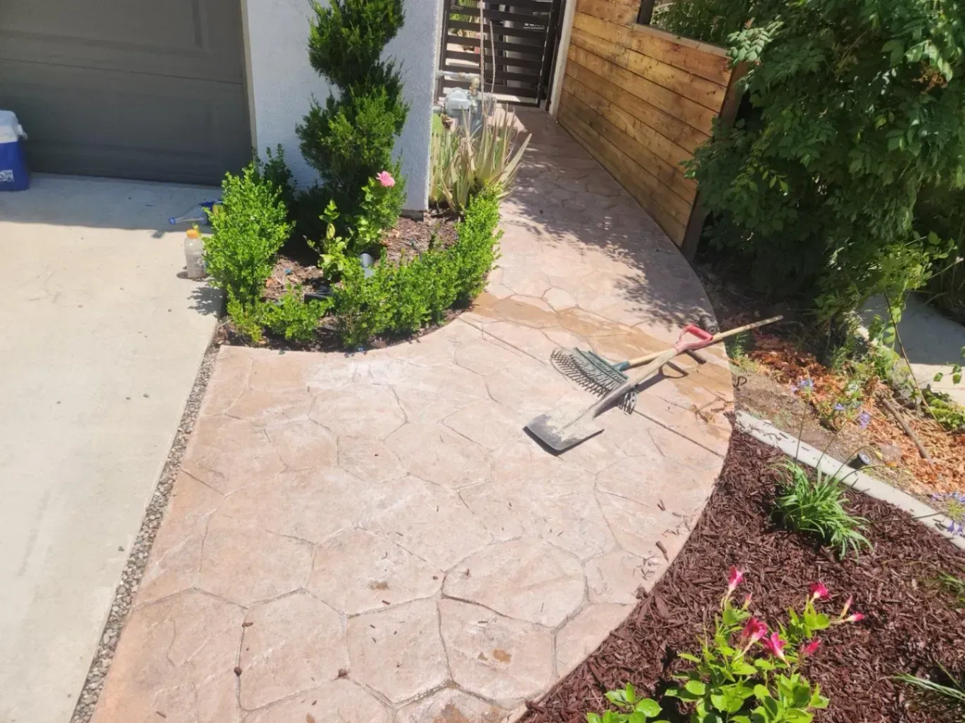 A stamped concrete pathway curves toward a gate; a small garden borders it.