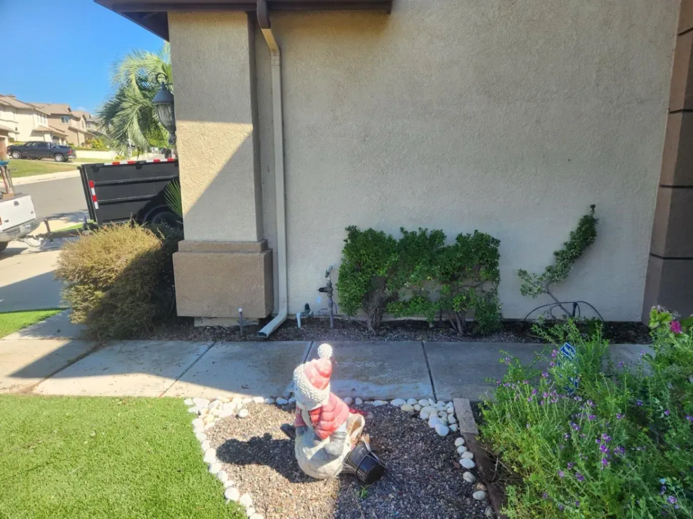 Gnome statue in a front yard garden with green grass, bushes, and a house in the background.