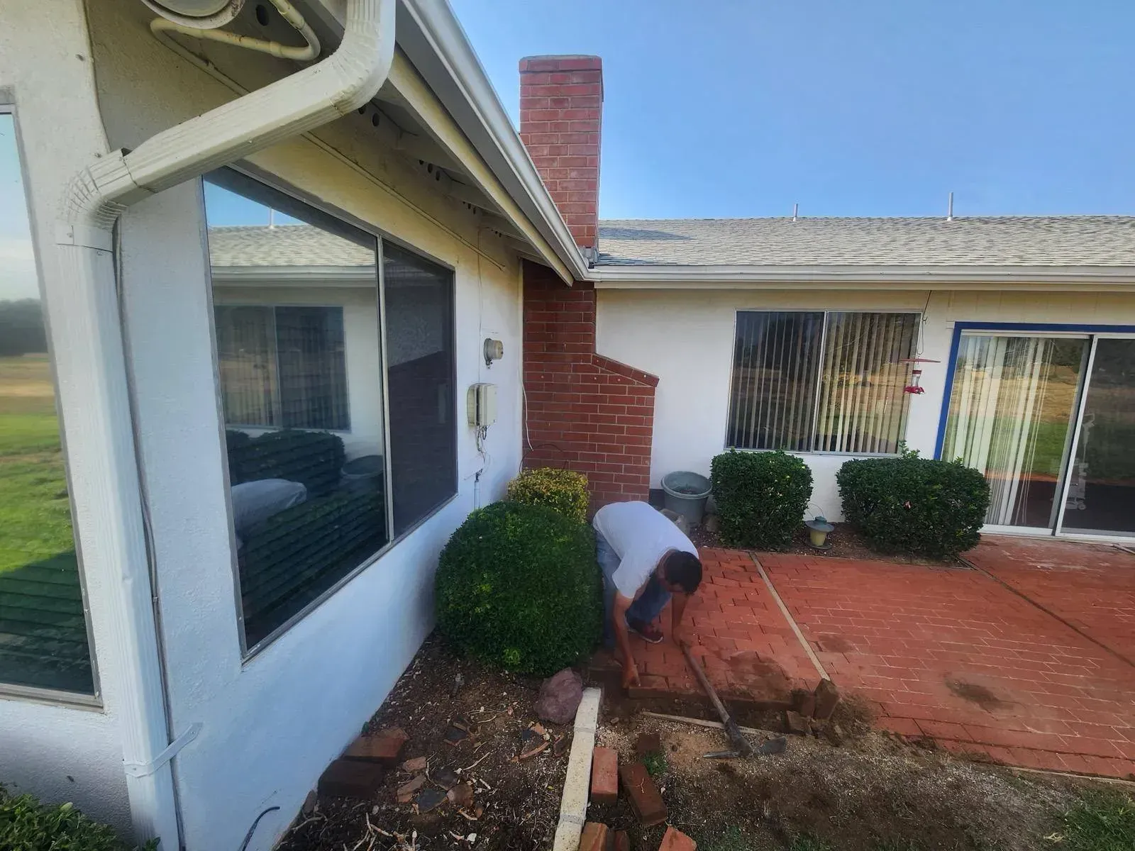 Person working in a yard near a house with windows and a brick chimney.