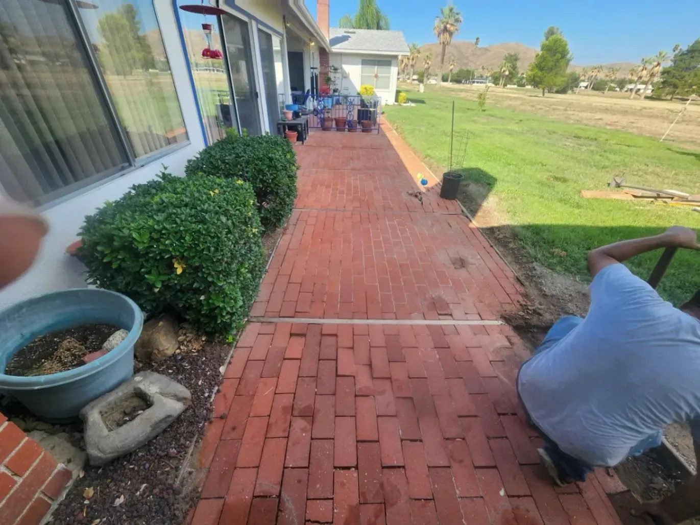 Red brick pathway beside a house and yard; a person sits on a chair near the edge.