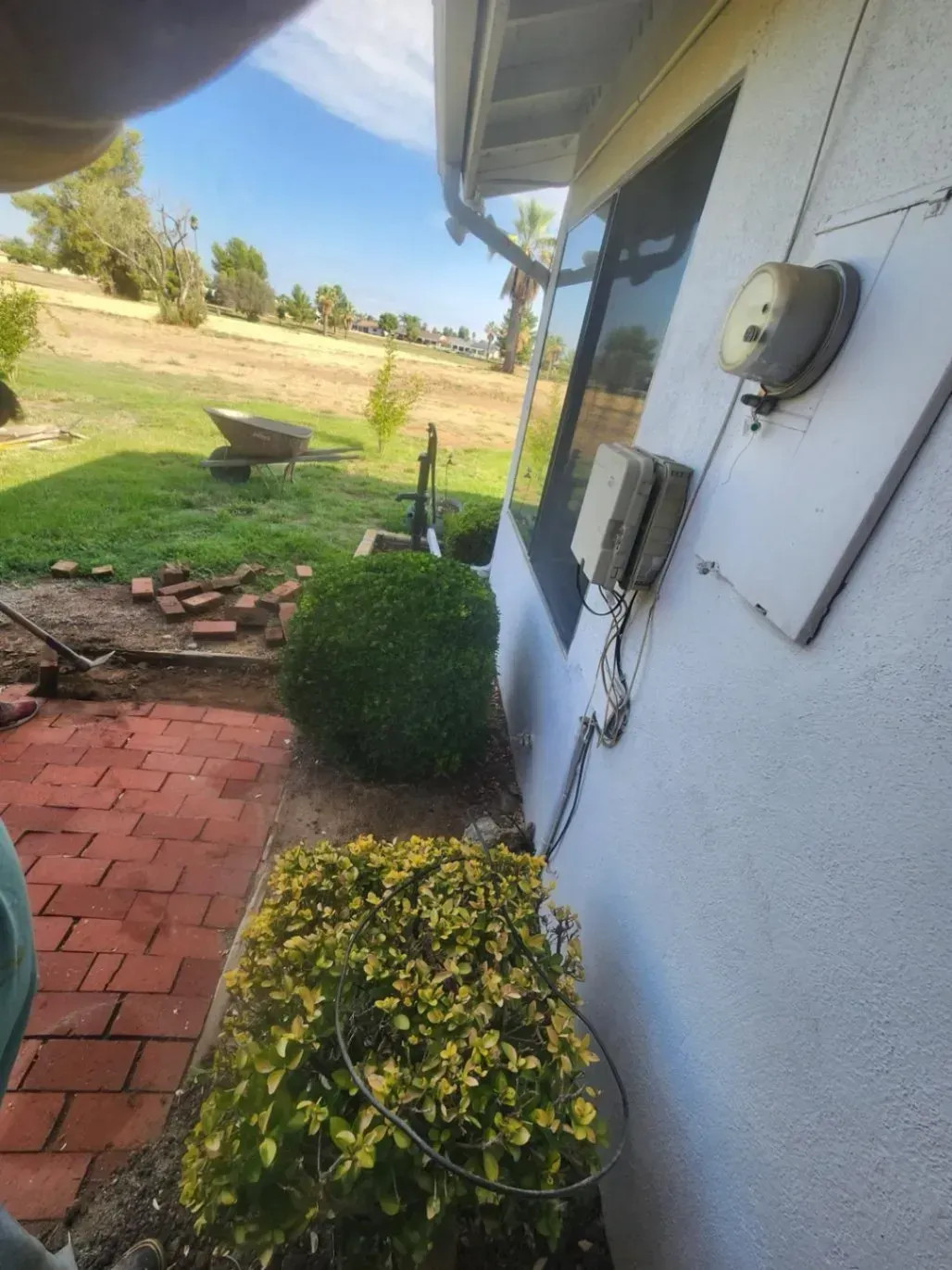 Side view of a house with a bush in front, next to a brick path and grassy yard.