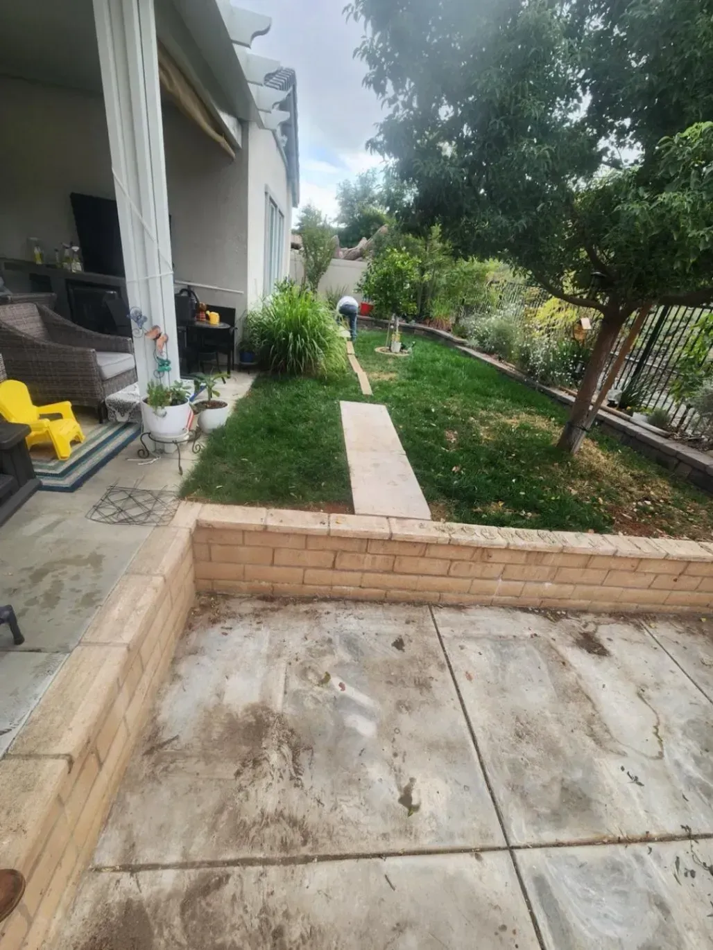 Patio with a brick retaining wall and a narrow grass path leading to a garden.