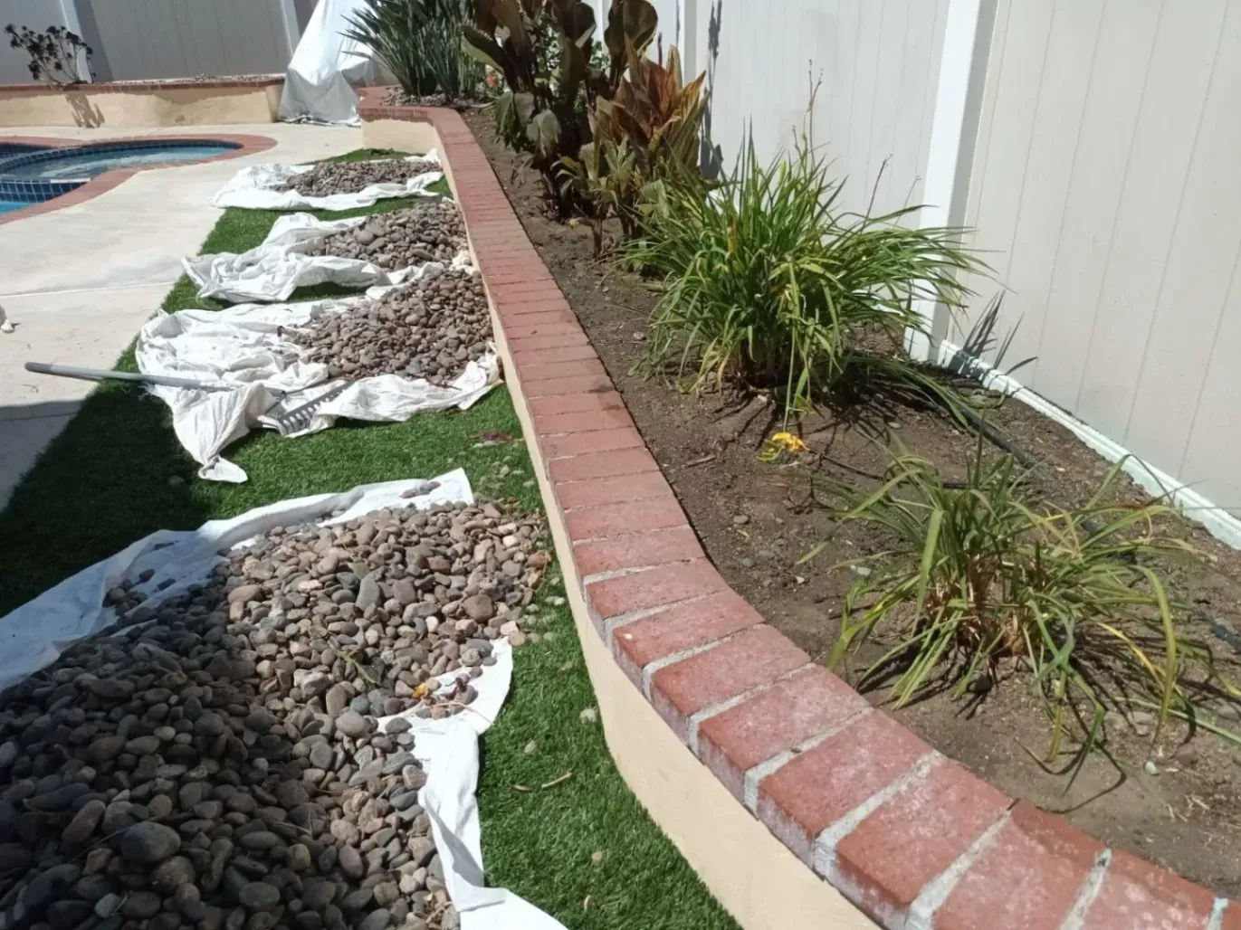 Landscaping with a brick border, plants, and gravel being poured on a white sheet.