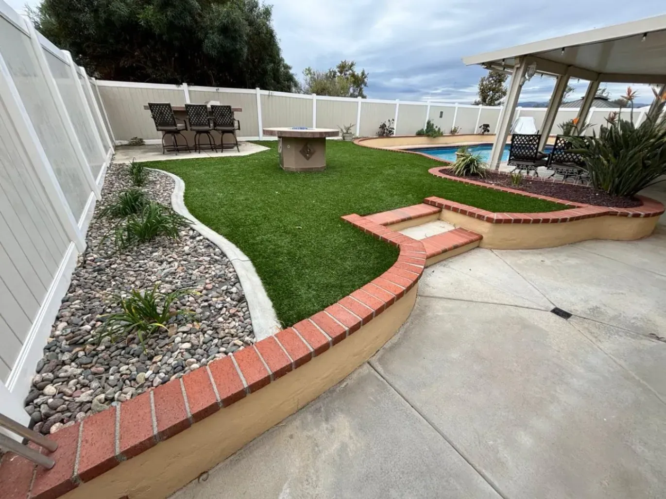 Backyard with artificial turf, pool, patio furniture, a fire pit, and white fence.