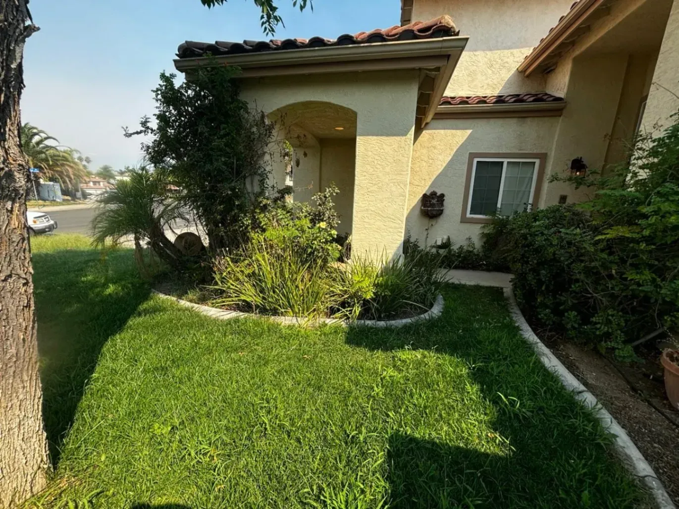 A house exterior with green lawn, front porch, and lush bushes.