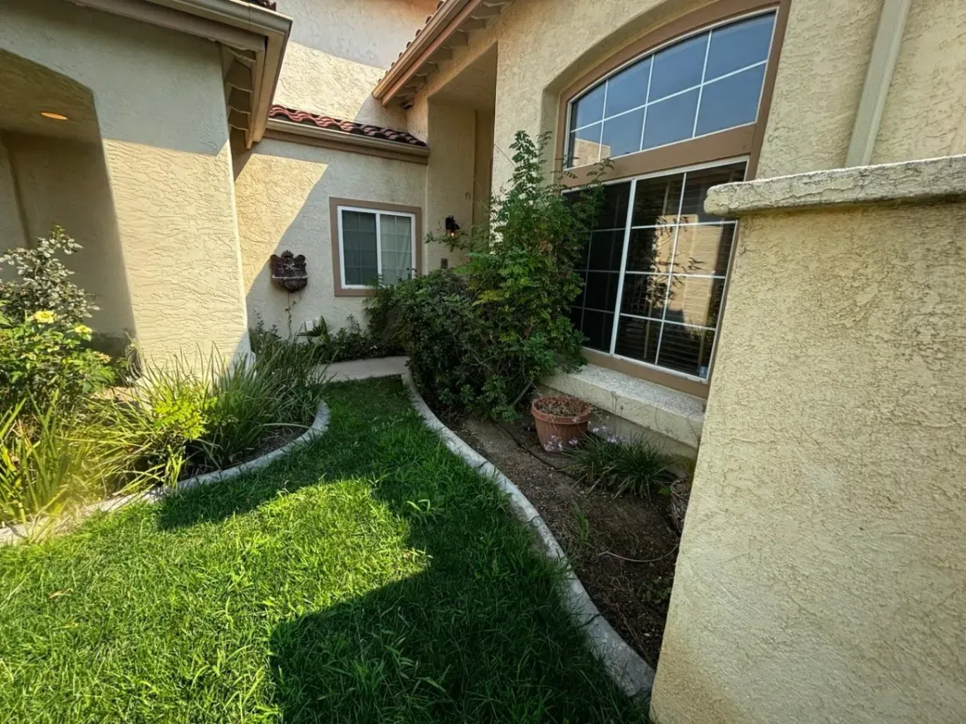 Green grassy walkway leading to a house entrance. Bushes grow along the path.
