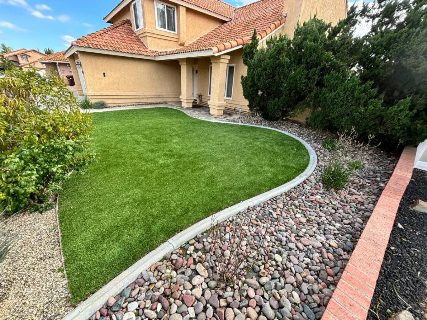 A house with artificial green lawn, concrete border, and rock garden.