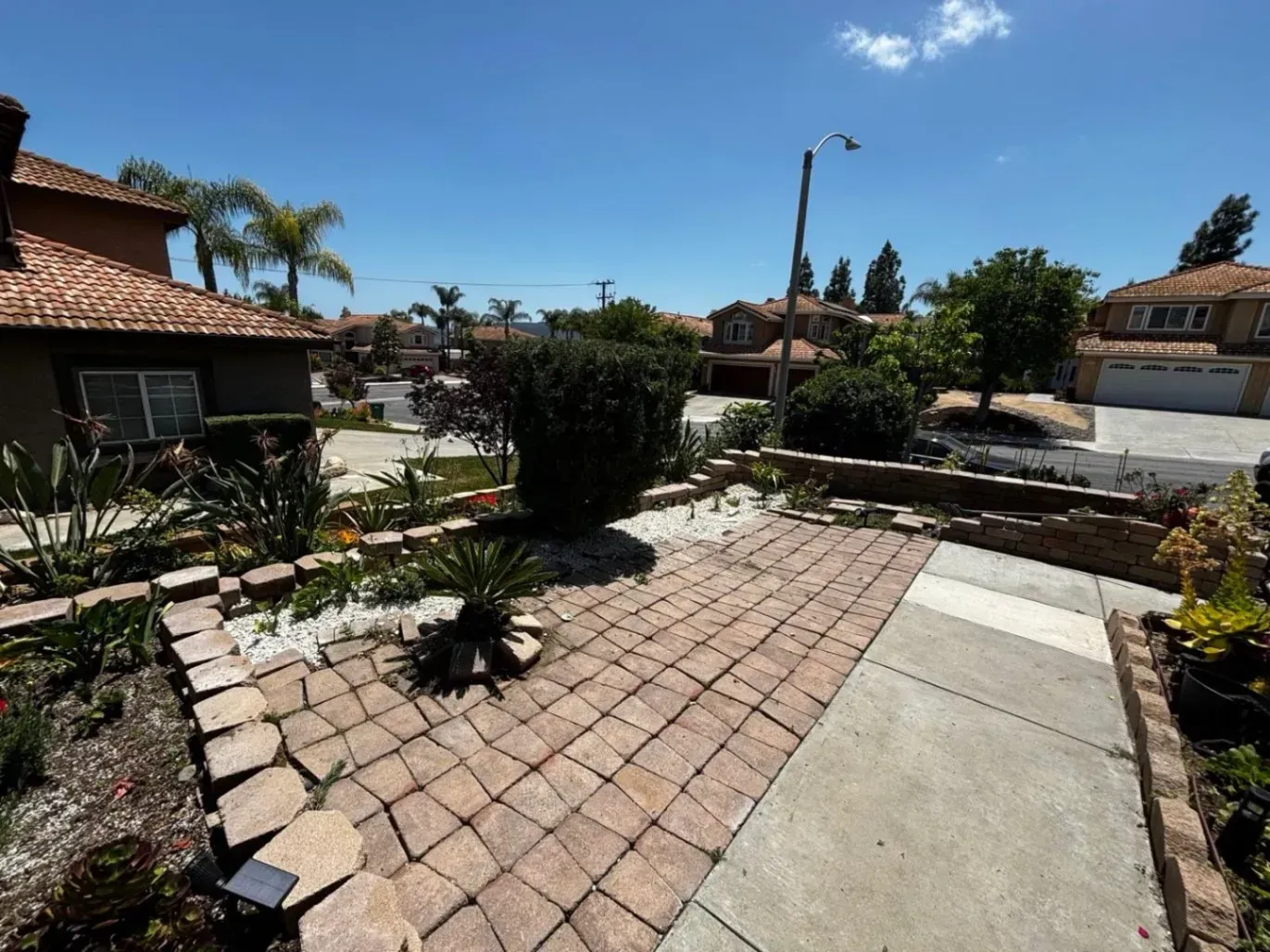 Brick patio and landscaped yard in front of a residential house on a sunny day.