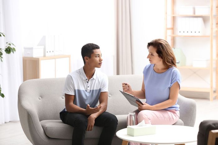 A woman is sitting on a couch talking to a young man.