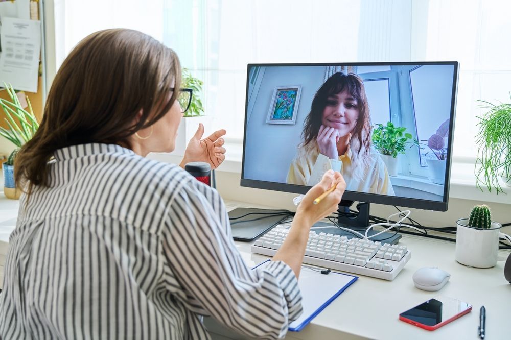 A woman is sitting at a desk talking to another woman on a video call.