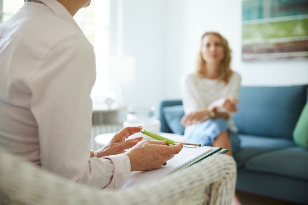 A woman is sitting on a couch talking to a doctor.