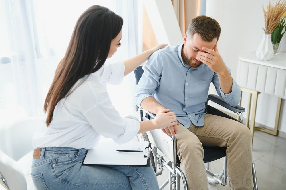 A woman is comforting a man in a wheelchair.