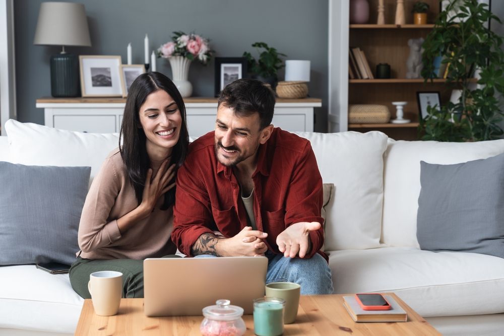 A man and a woman are sitting on a couch looking at a laptop.