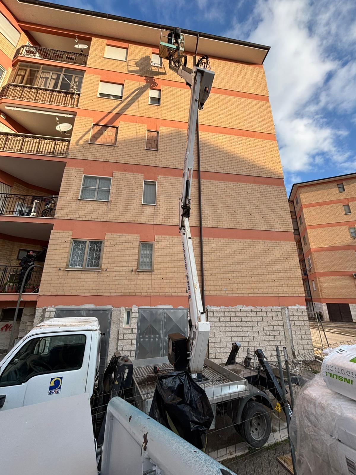 Una piattaforma aerea montata su un camion si è estesa fino a raggiungere il tetto di un edificio residenziale in mattoni a più piani, sotto un cielo azzurro.