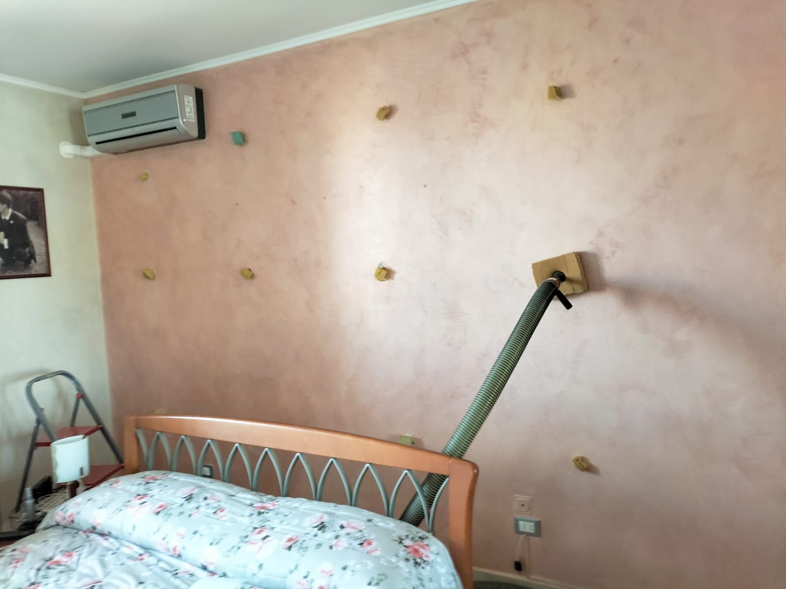 Una parete rosa dietro un letto con dei blocchi di legno fissati e un tubo flessibile che va dal letto alla parete.