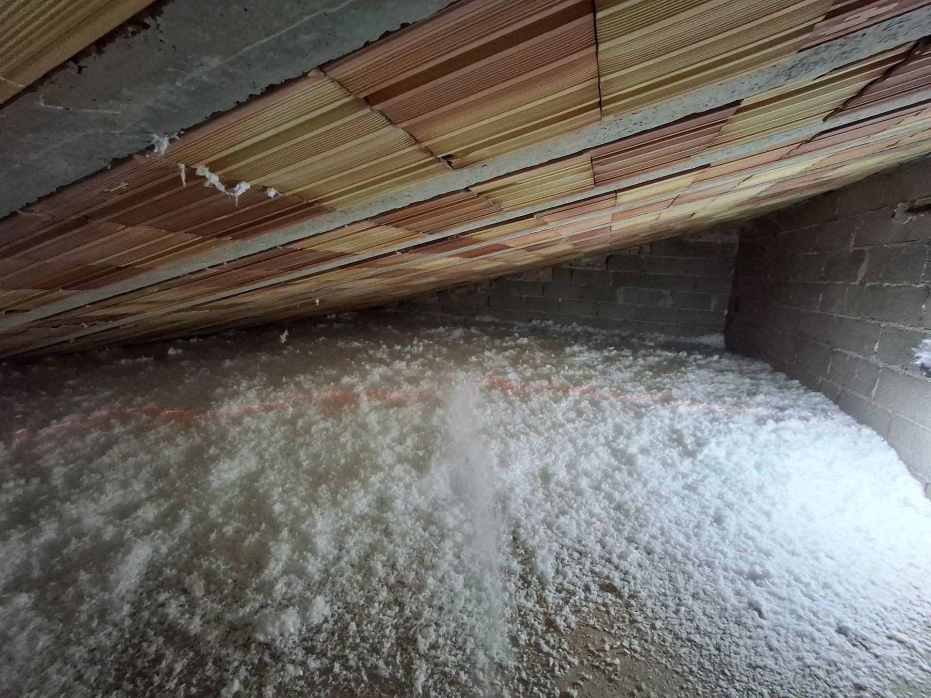 Una soffitta che mostra le travi in ​​legno e il tetto sopra uno spesso strato di isolante bianco sfuso.
