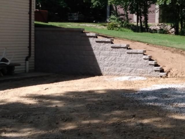 A stone wall is being built in the backyard of a house.
