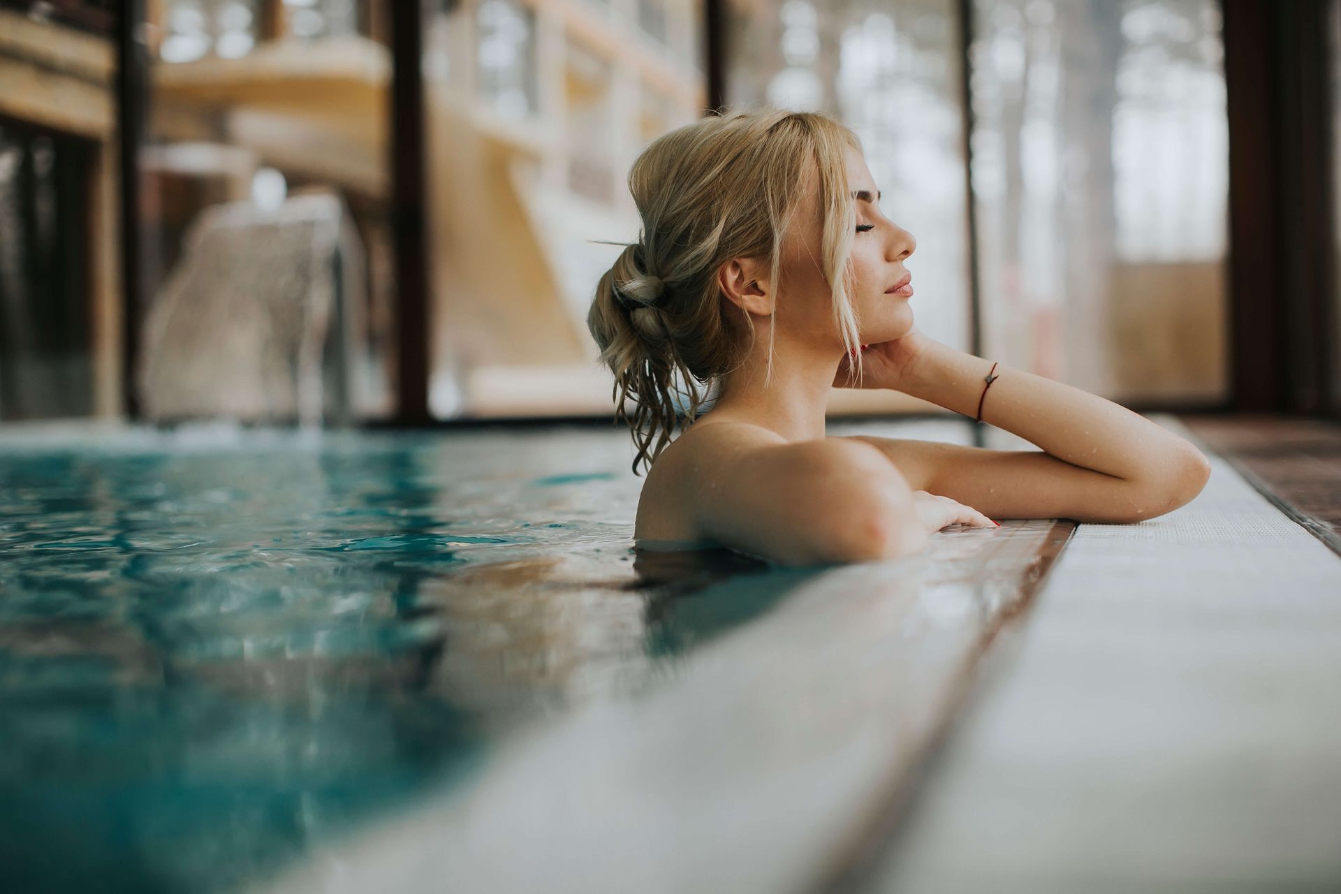 A woman is sitting in a swimming pool with her eyes closed.