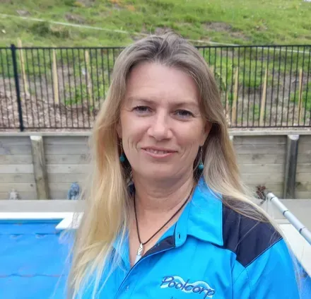 A woman in a blue shirt is standing in front of a pool.
