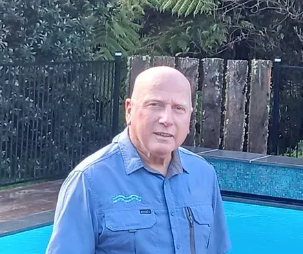 A bald man in a blue shirt is standing next to a swimming pool.