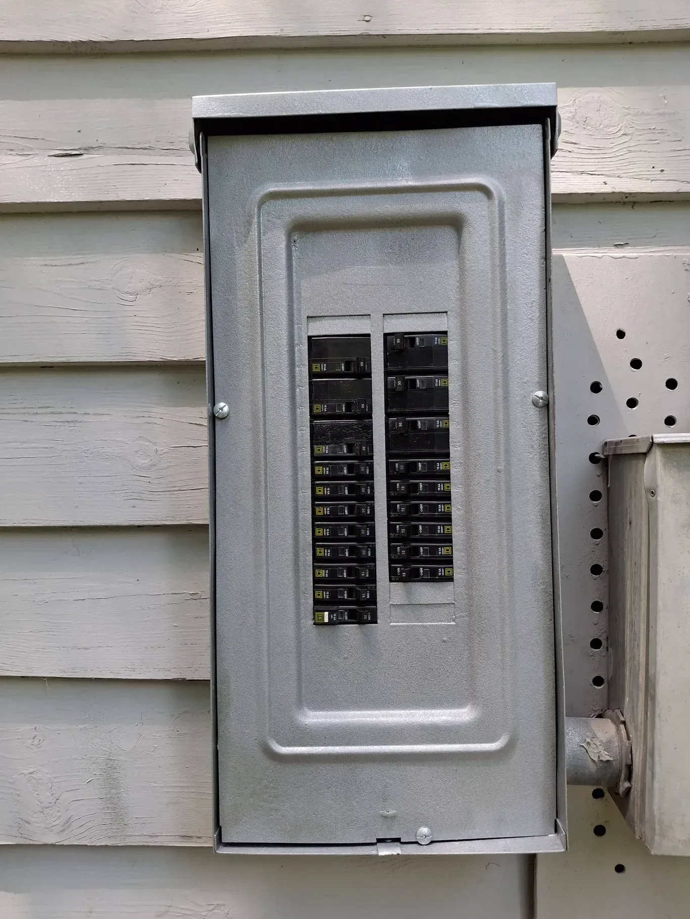 Metal electrical breaker box mounted on white siding.