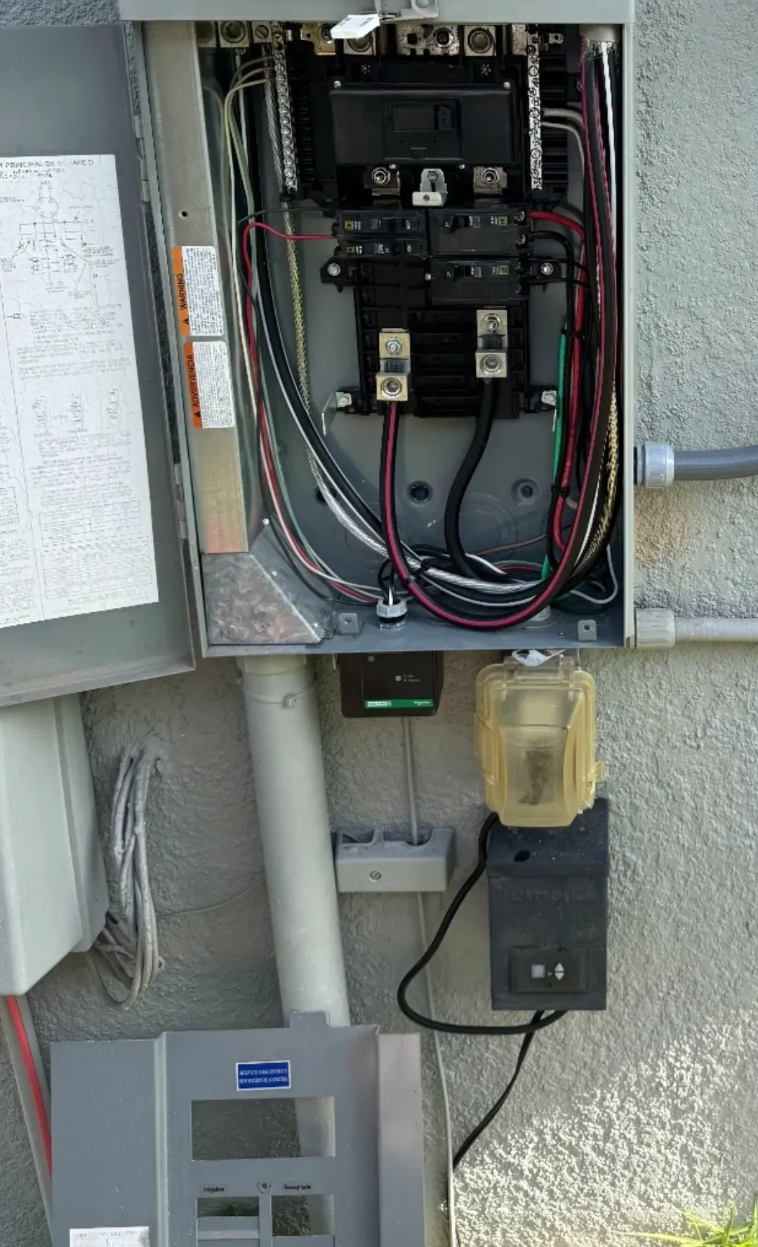 Electrical box with wires, conduits, and attached devices on a wall.