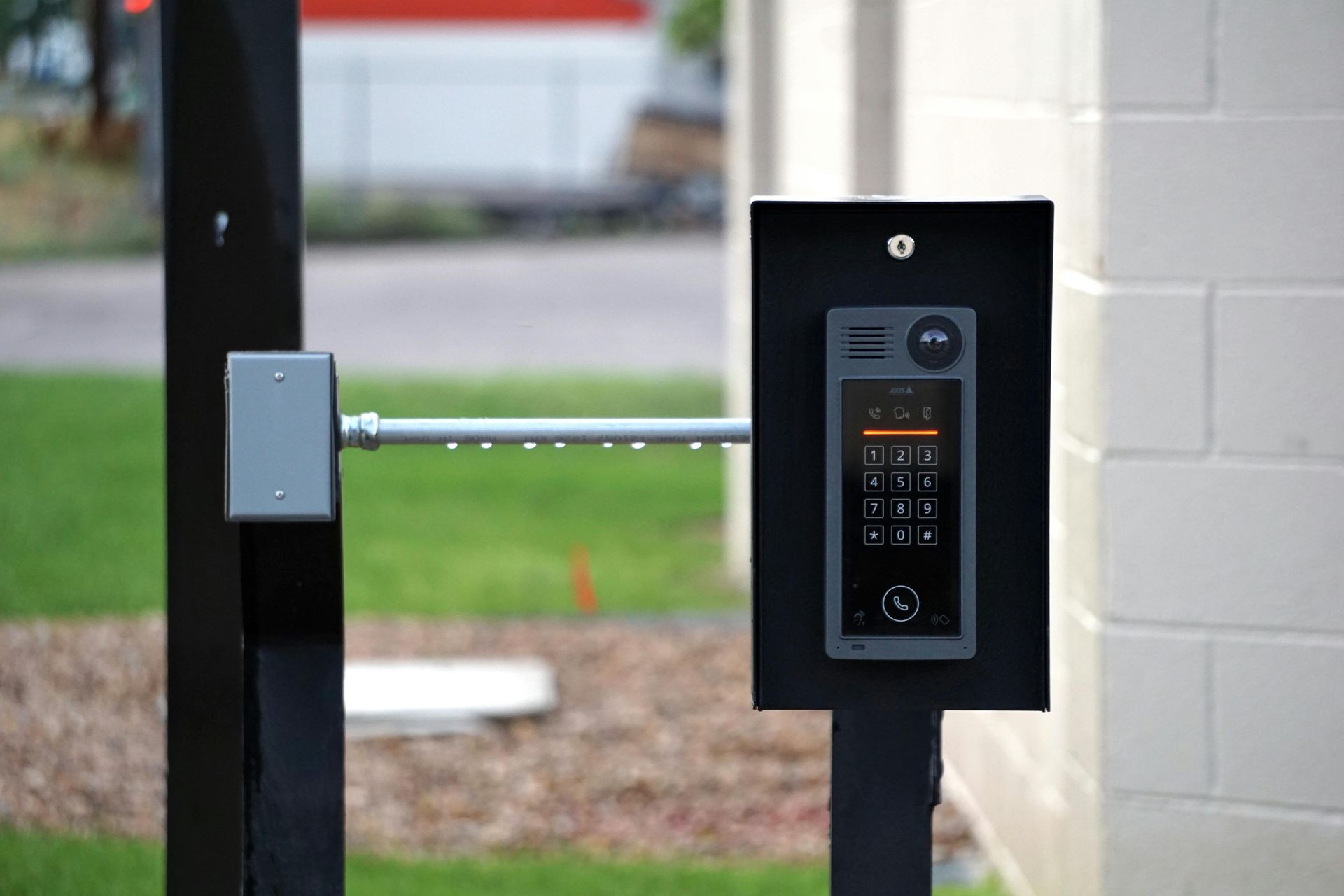 Black entry system with keypad and display on a post near a white brick wall.