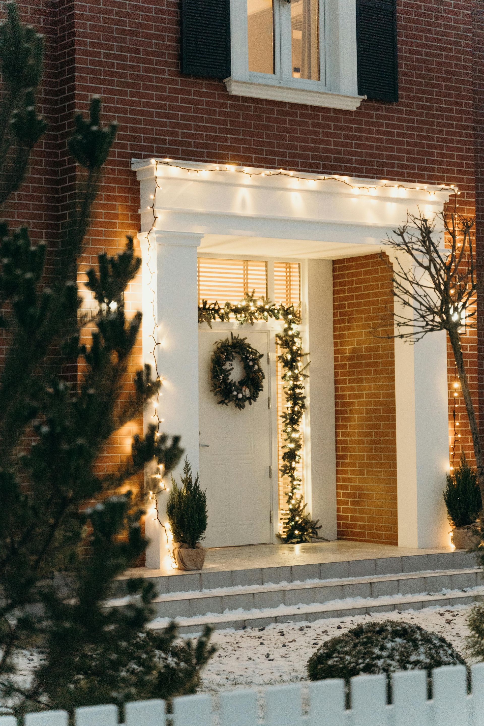 Red brick house with Christmas decorations, including lights, wreath, and garland on the front entrance.