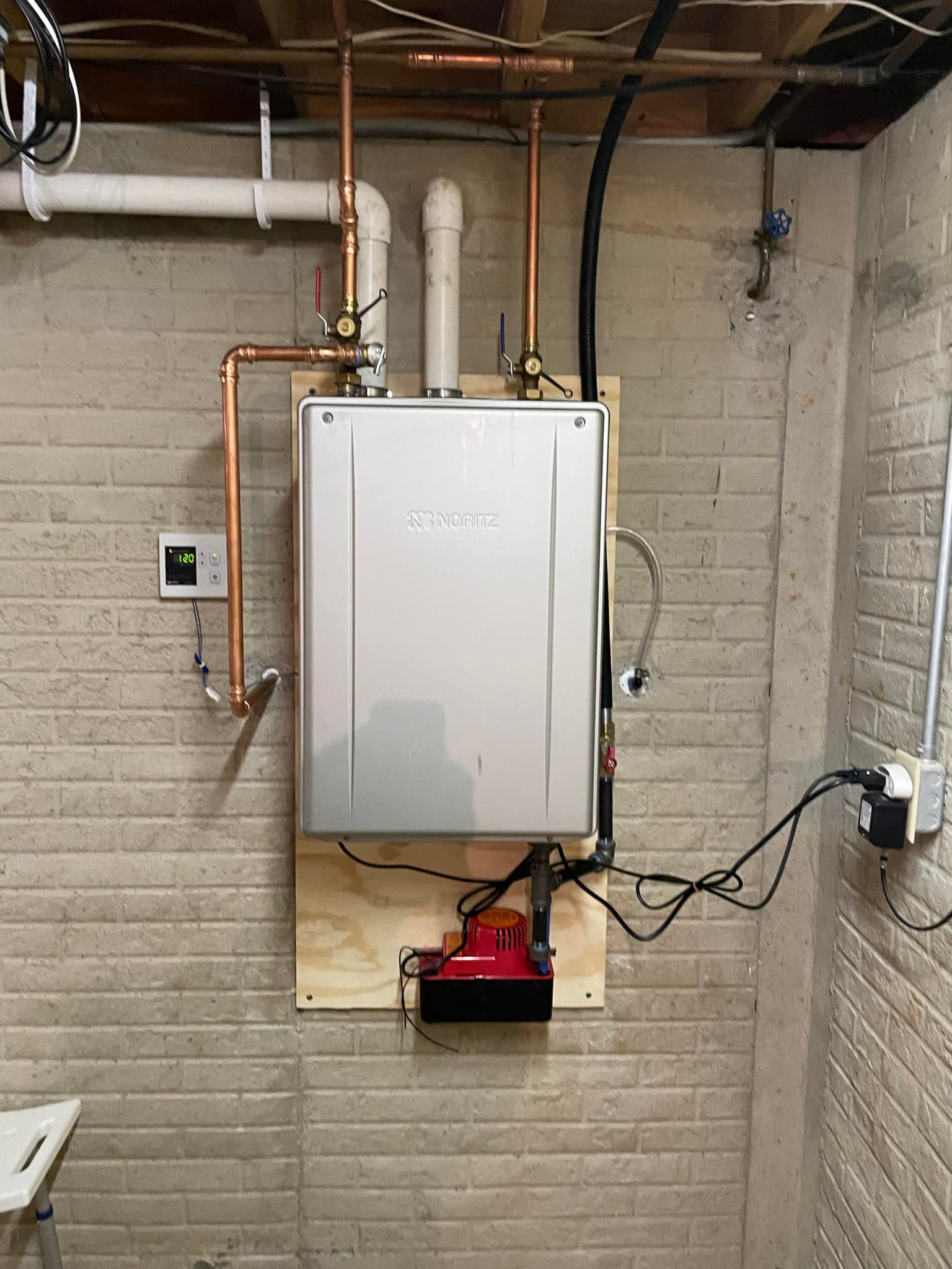 A water heater is mounted to a brick wall in a basement.