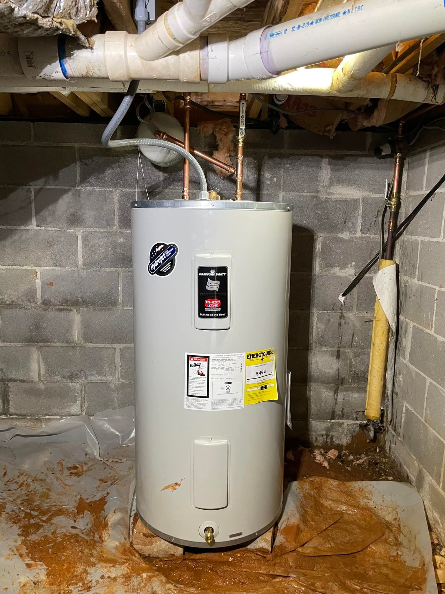A water heater is sitting in a basement next to a brick wall.