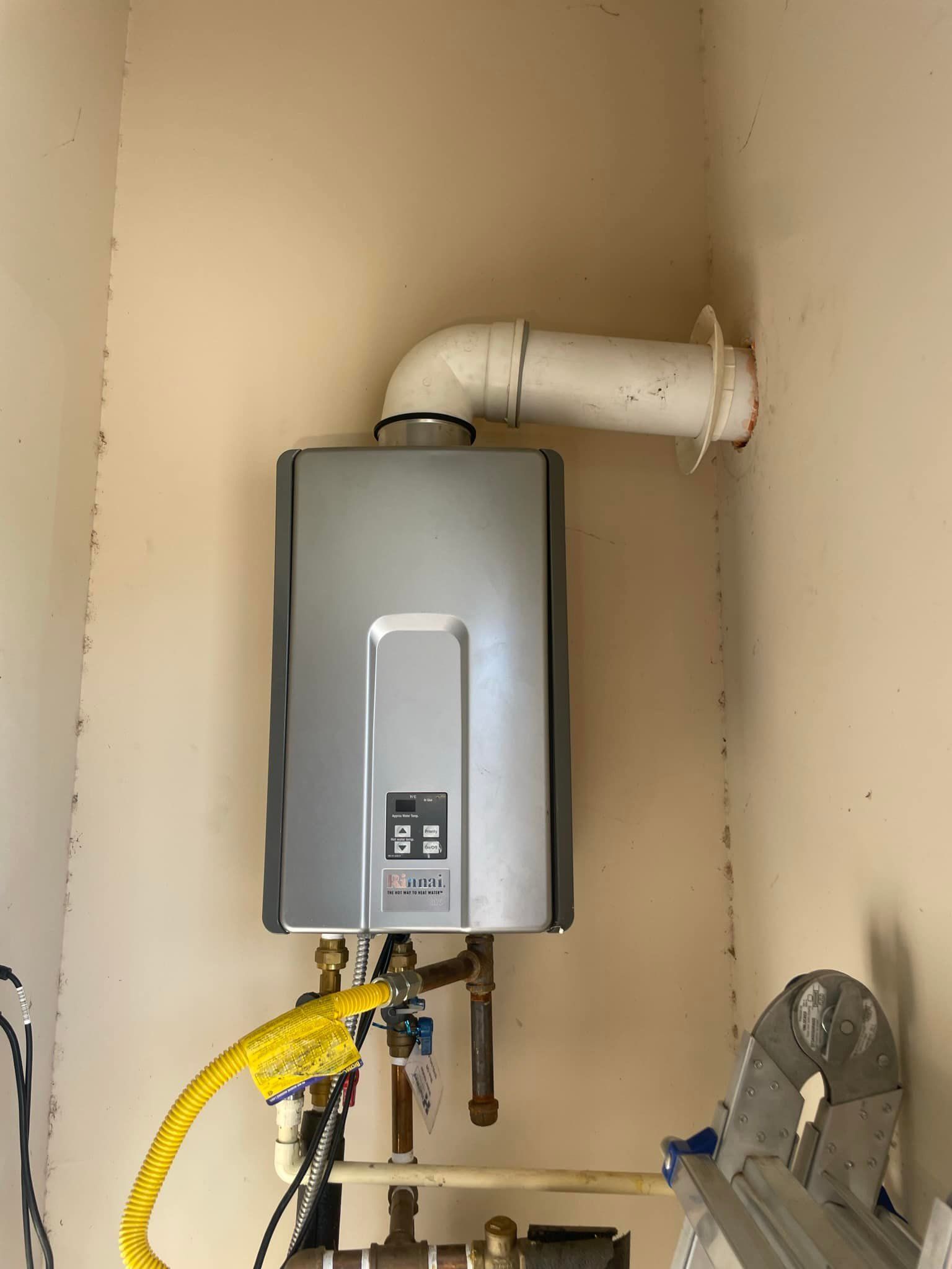 A water heater is hanging on a wall next to a ladder.