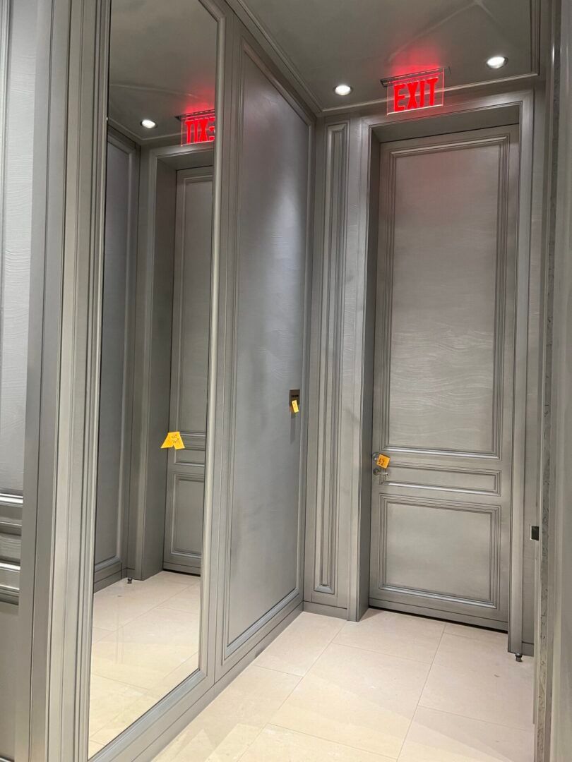 A hallway with two doors and a red exit sign.