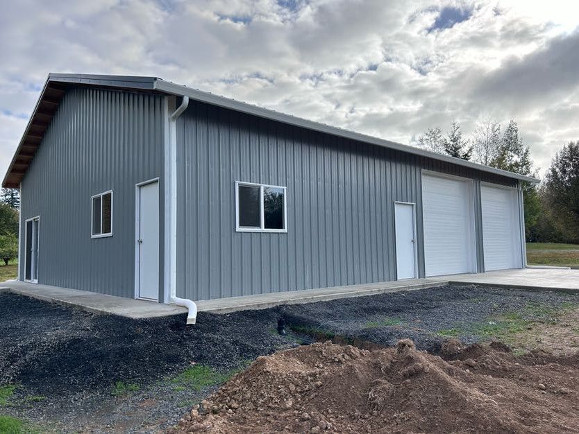 A large gray metal building with white doors and windows is sitting on top of a dirt field.