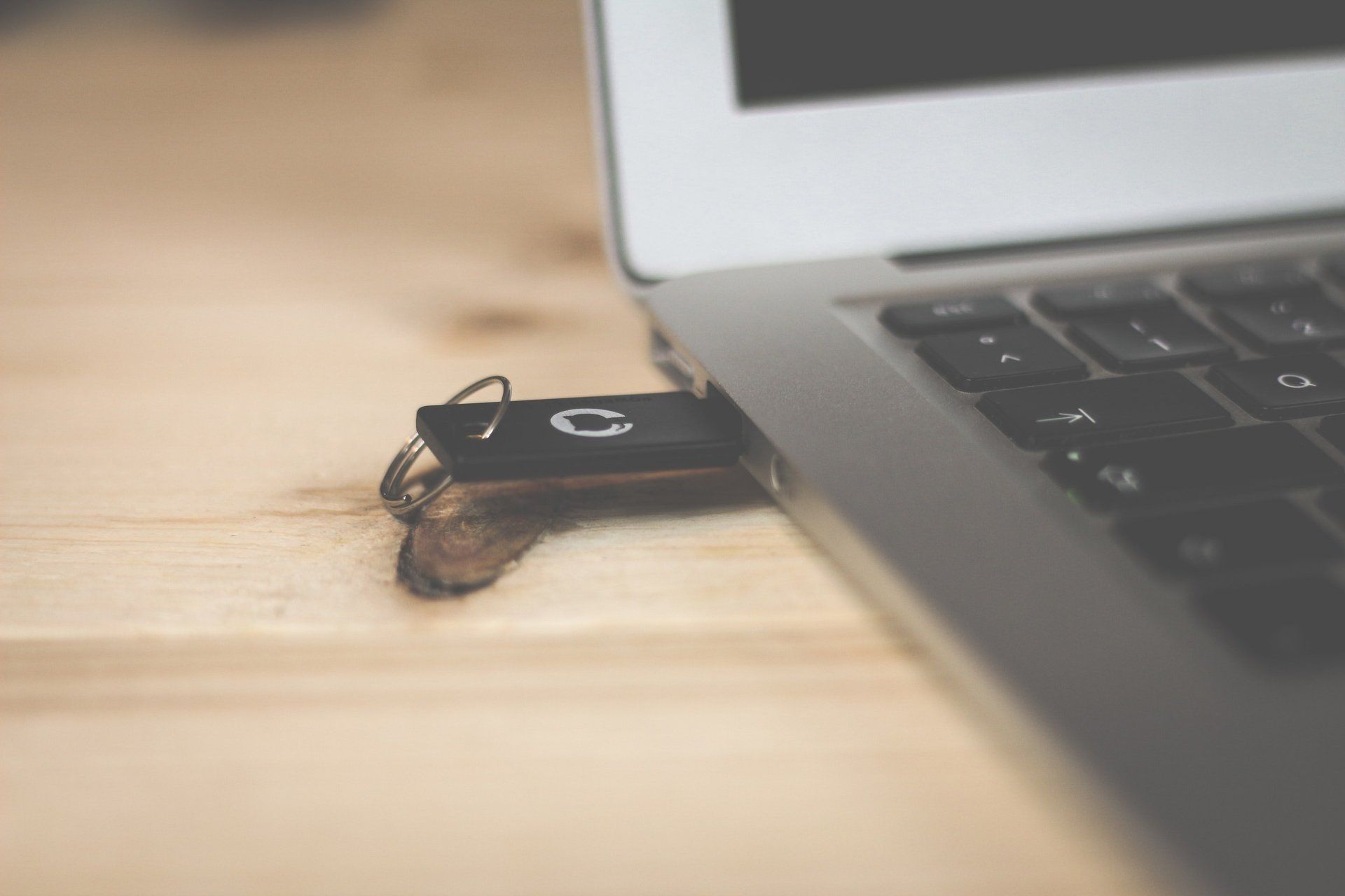 A flash drive is plugged into a laptop on a wooden table.