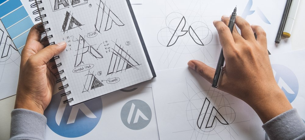 A person is drawing a logo in a notebook with a pen.