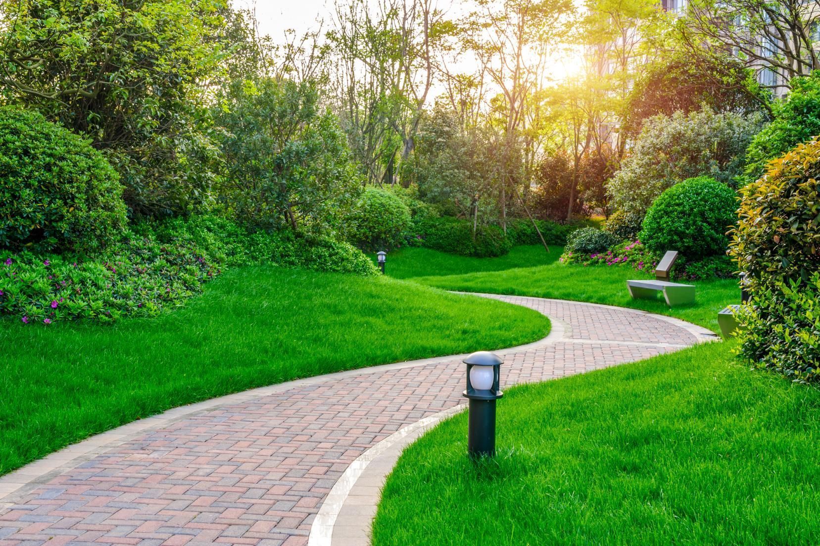 A brick walkway in a park surrounded by green grass and trees.