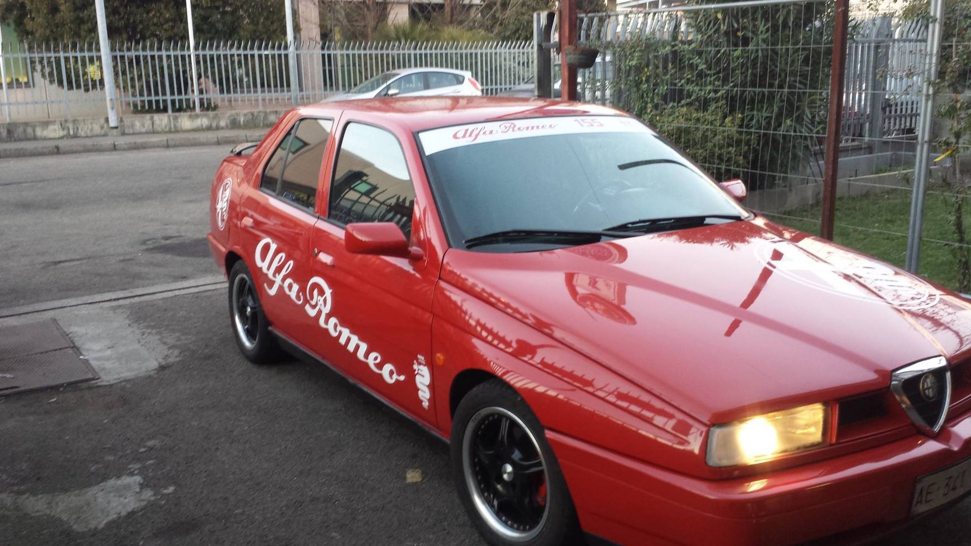 Berlina Alfa Romeo rossa con cerchi neri parcheggiata su una strada. Adesivo