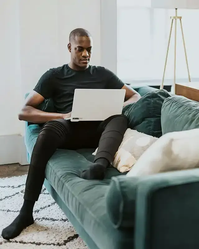 A man is sitting on a couch using a laptop computer.