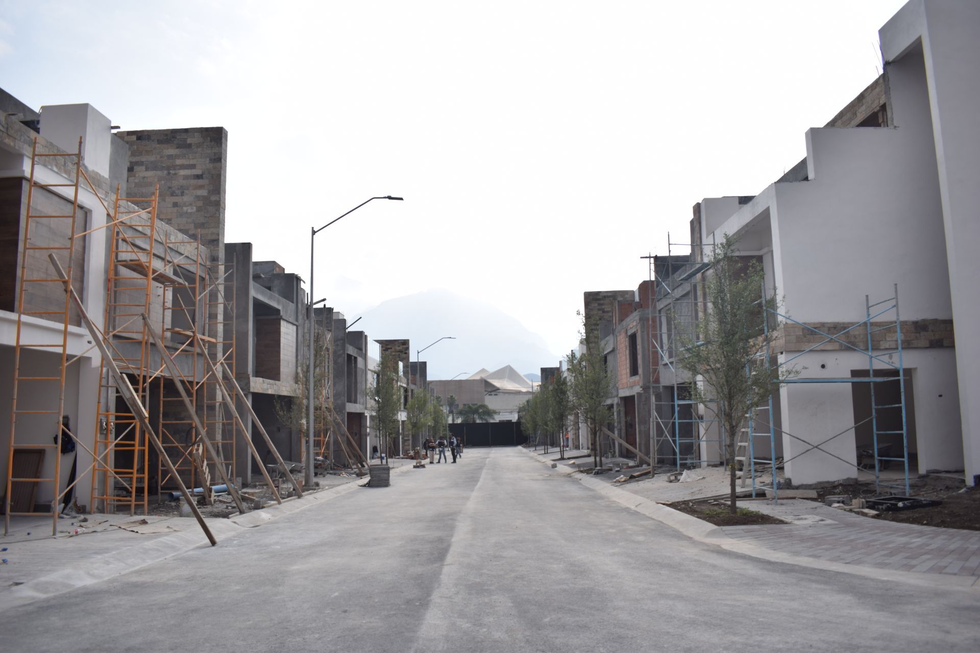 Calle residencial vacía con casas sin terminar y andamios a ambos lados.