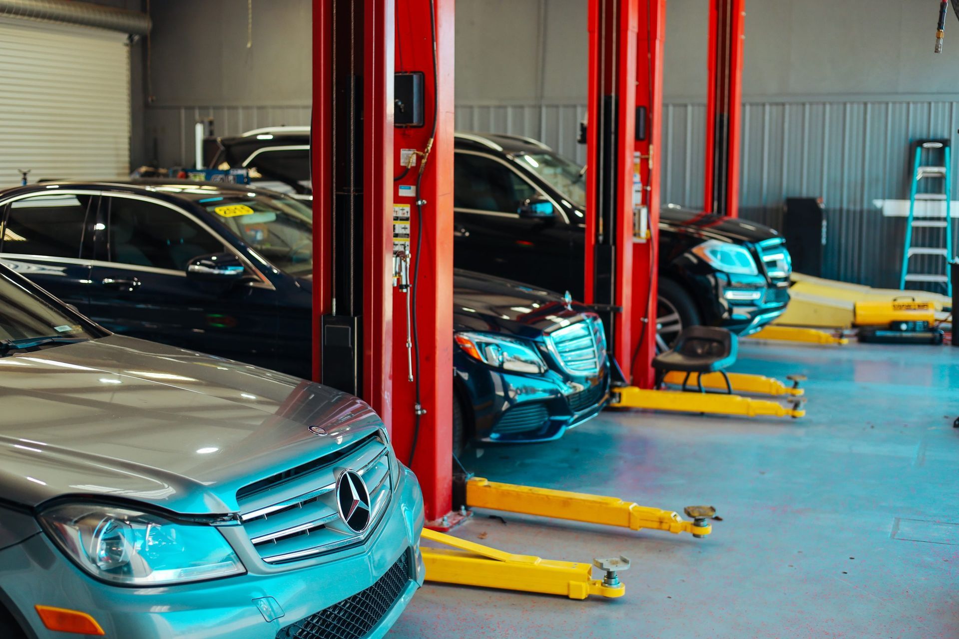 A row of cars are parked on hydraulic lifts in a garage. | Redline Automotive