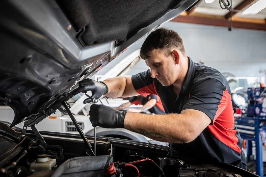 A man is working on the engine of a car with the hood up. | Redline Automotive