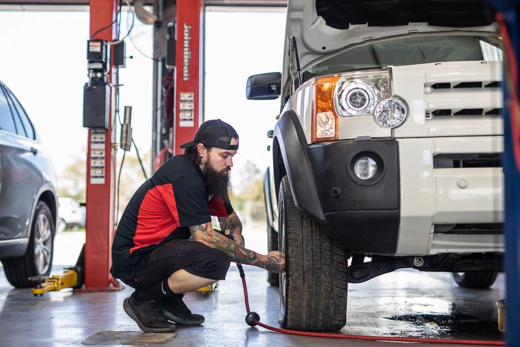 A man is kneeling down to change a tire in a garage. | Redline Automotive