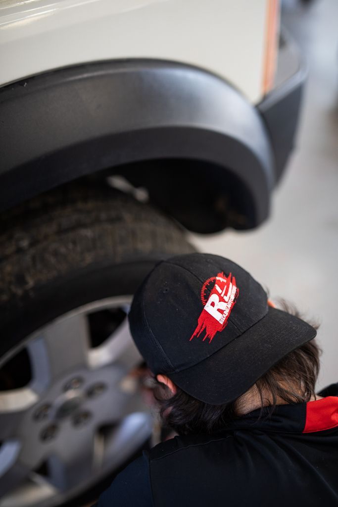 A man wearing a black hat is working on a car tire. | Redline Automotive